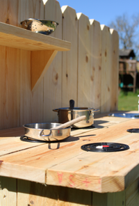Outdoor cooking setup with pots and pans on a wooden surface against a wooden fence.
