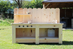 Wooden outdoor kitchen with shelves and cooking utensils on a grassy area.