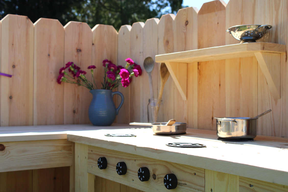 Outdoor kitchen setup with wooden counter, pots, pans, and a vase of flowers.