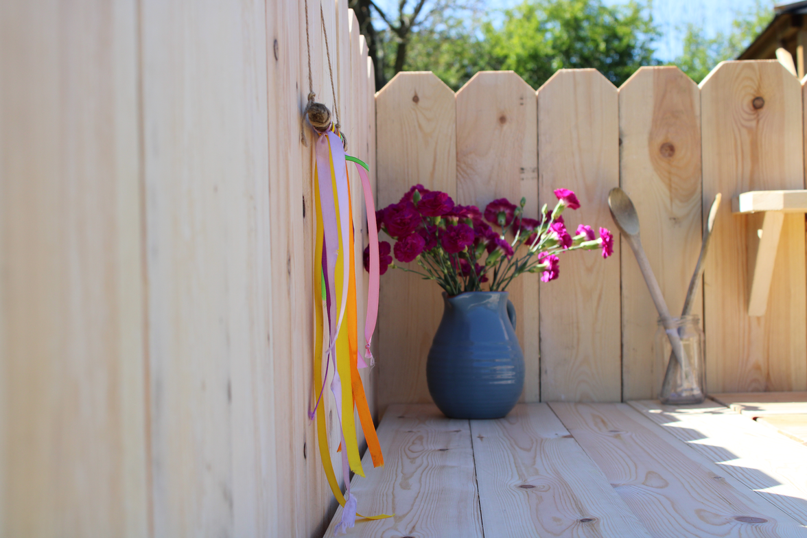 Vase with flowers against a wooden fence on a sunny day