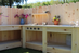 Wooden outdoor play kitchen with shelves and decorative elements against a wooden fence.