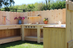Wooden outdoor kitchen with sinks and shelves against a wooden fence.