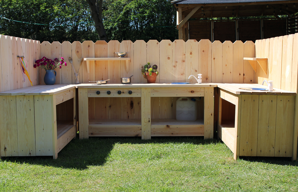 Wooden outdoor kitchen setup with cabinets and countertops in a backyard.